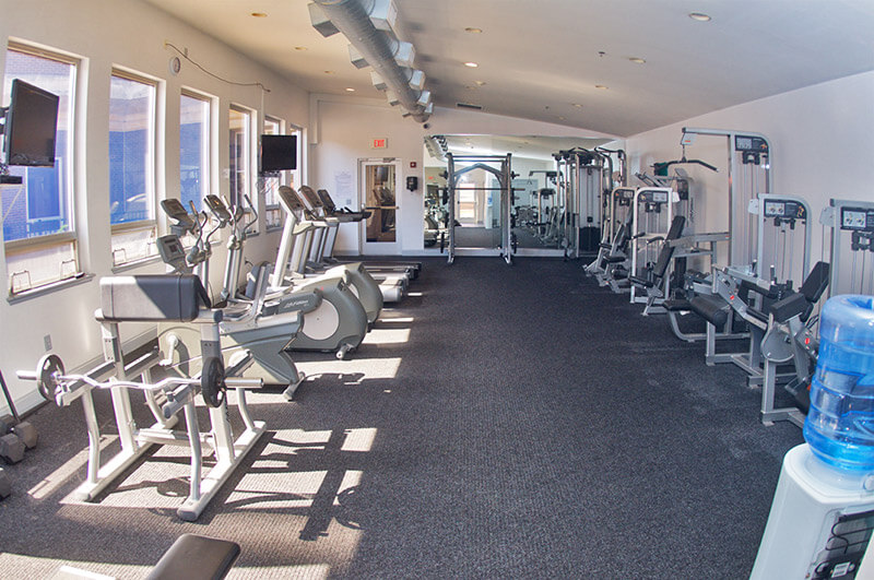 A photo of the Metroclub condominium building's gym. A variety of exercise equipment, including weight benches, eliptical machines, and more are pictured.