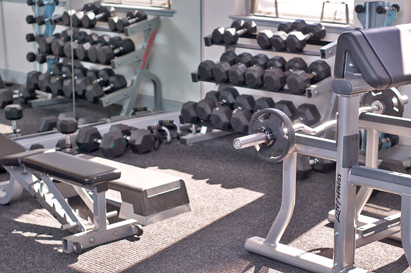 A photo of the Metroclub condominium building's gym. A variety of hand weights and weight benches are pictured.